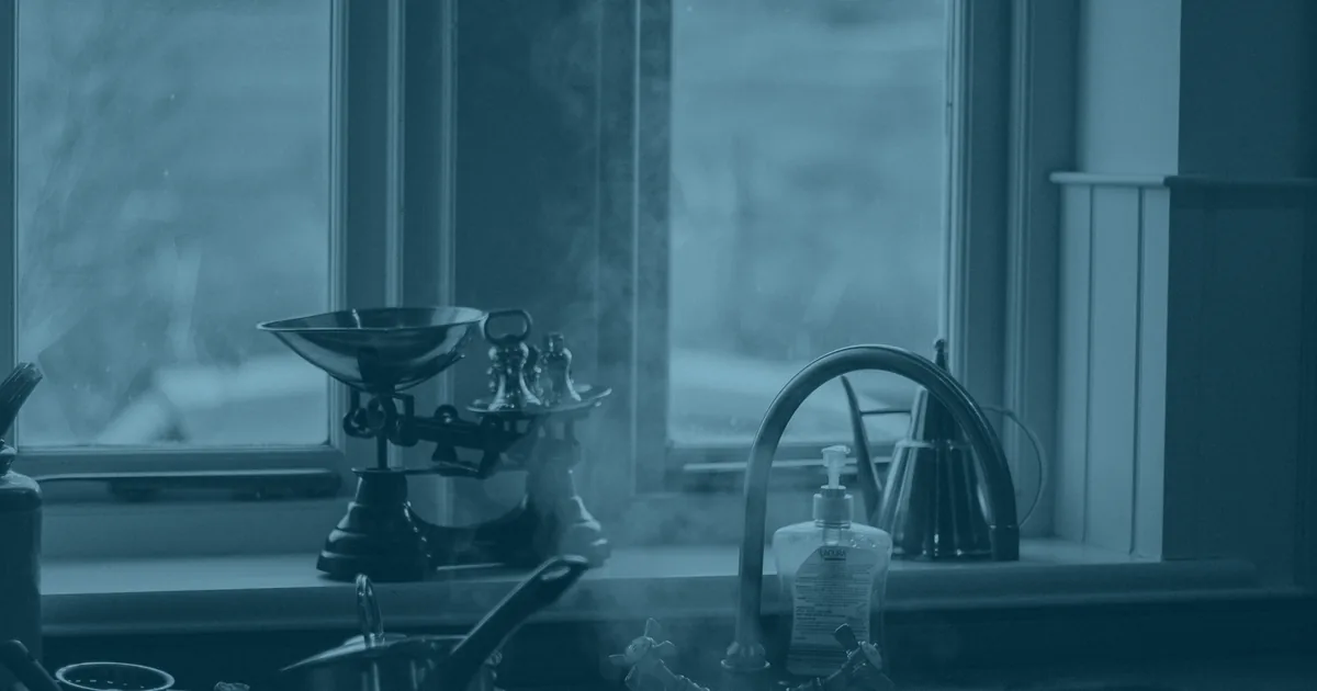 Steam drifting across a kitchen window that looks out over open countryside, with an old set of scales and a kettle on the sill.