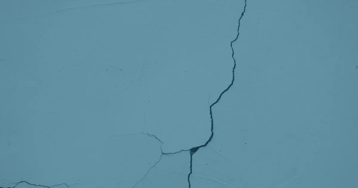 A long crack running down a painted plaster wall, branching into finer cracks near the bottom.