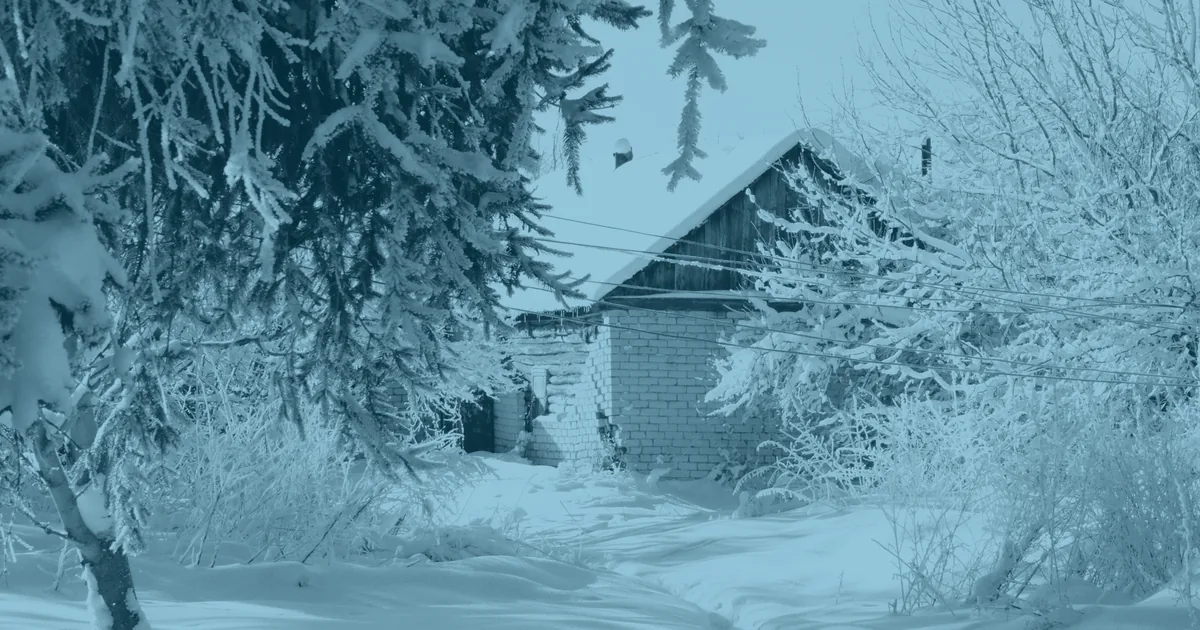 A small house standing in deep snow, seen past heavily frosted branches.