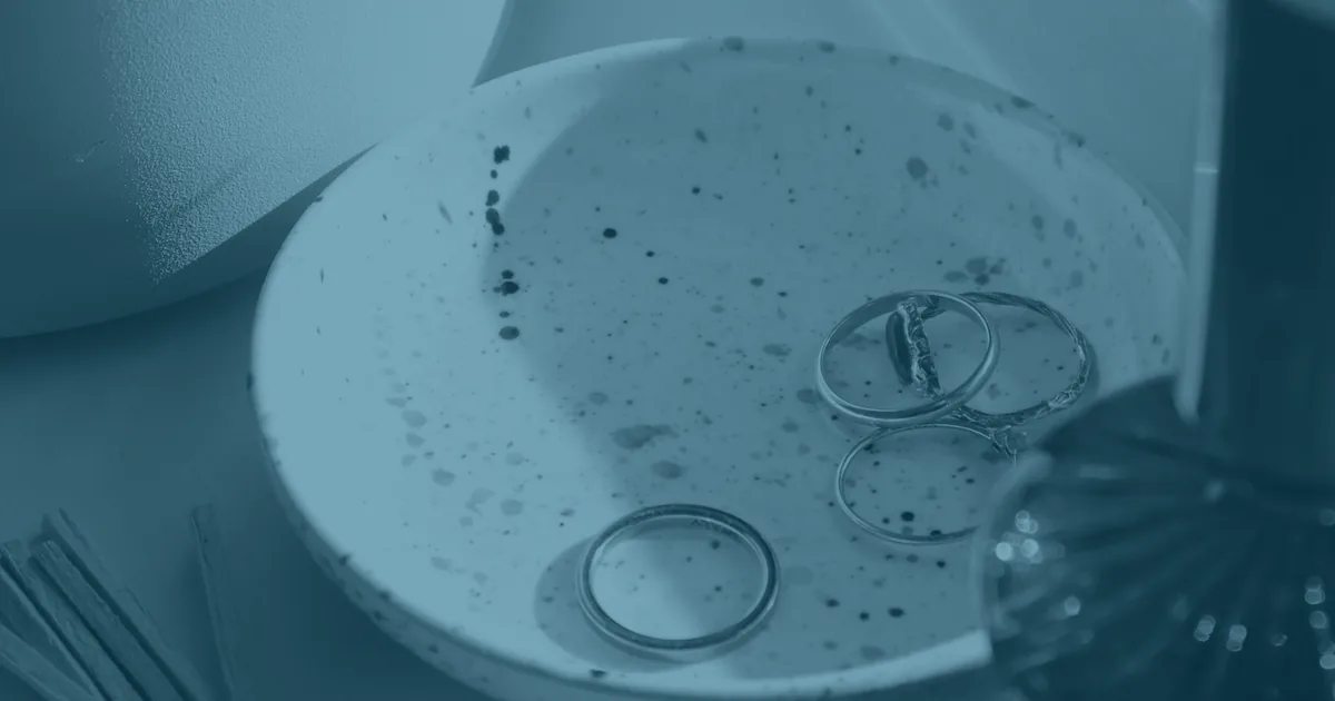 A speckled ceramic dish holding a few rings, with one plain band lying apart from the cluster of others.